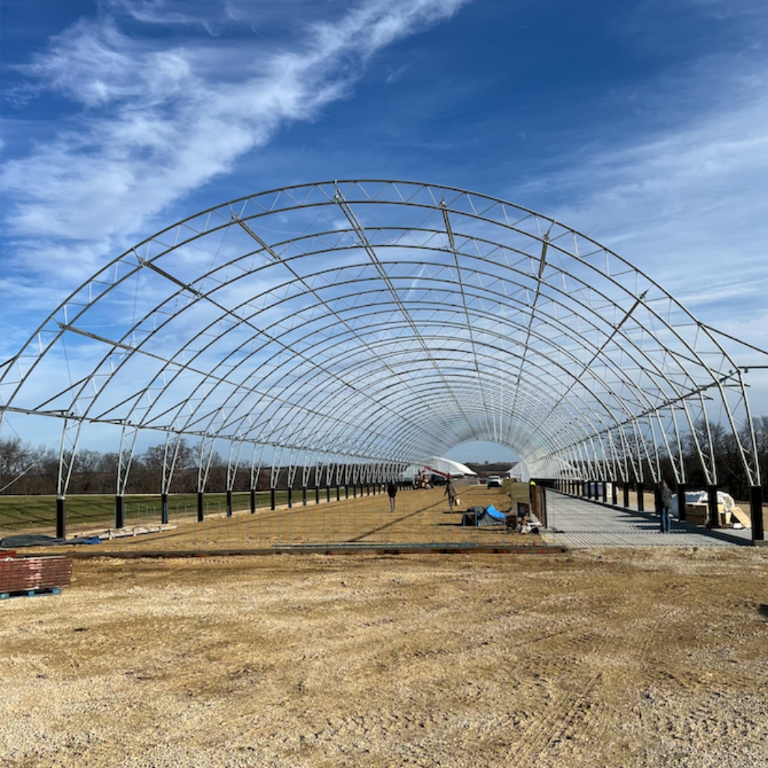 A professional construction crew assembling a large white fabric hoop building frame on a clear day, demonstrating expert installation techniques and teamwork.