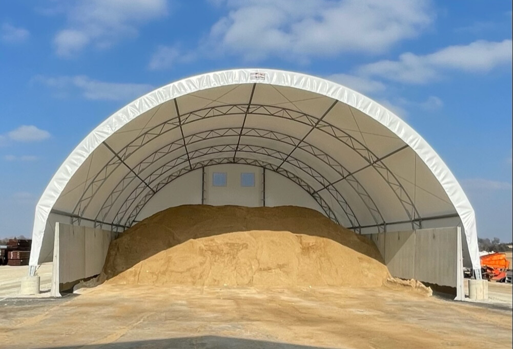 Large fabric hoop building storing road salt and sand, featuring a protective covered structure designed for municipal winter material storage